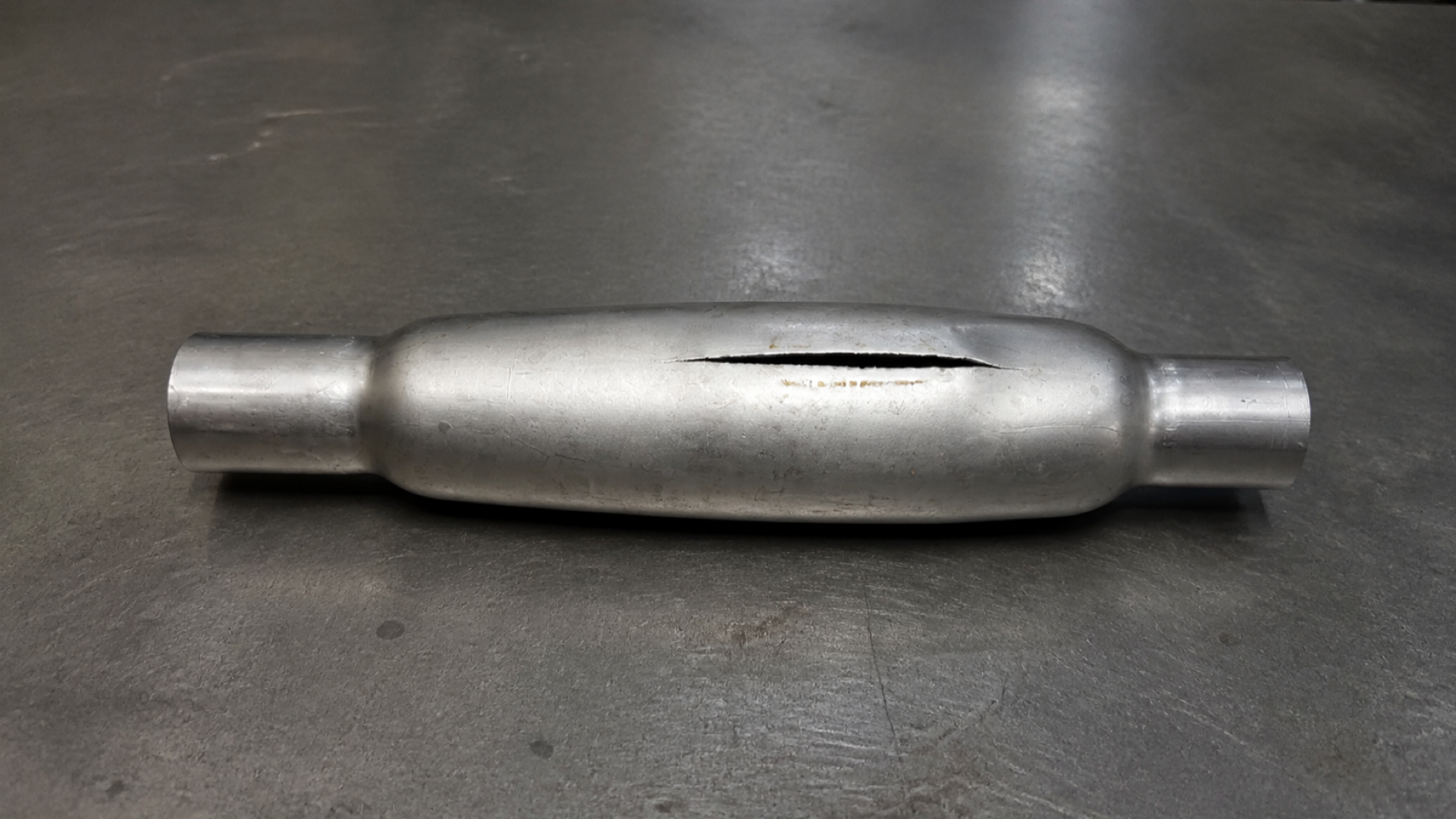 Hydroformed tube specimen with a longitudinal split on a steel workbench.